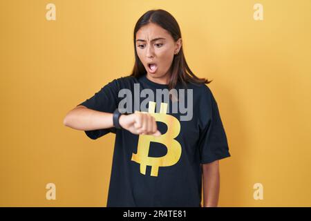 Jeune femme hispanique portant un t-shirt bitcoin regardant l'heure de montre inquiet, peur de se mettre en retard Banque D'Images