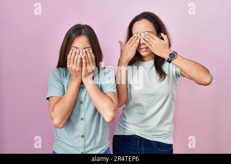 La jeune mère et la fille se tenant sur fond rose frottant les yeux pour la fatigue et les maux de tête, l'expression endormie et fatiguée. problème de vision Banque D'Images