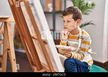 Enfant blond dessinant avec expression de doute au studio d'art Banque D'Images