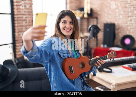 Une jeune femme hispanique musicienne fait selfie par smartphone tenant ukulele au studio de musique Banque D'Images