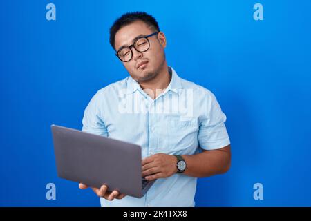 Jeune homme chinois utilisant un ordinateur portable qui a l'air endormi et fatigué, épuisé pour la fatigue et la gueule de bois, les yeux paresseux le matin. Banque D'Images