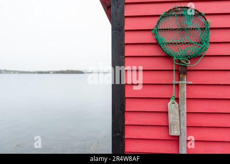 Un filet de pêche vintage accroché sur un mur de claquettes horizontal en bois rouge vif. La pelle est rouillée et le filet de corde de maille de tissu est déchiré et usé Banque D'Images