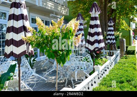 Plusieurs tables et chaises vides en fer forgé blanc sur la terrasse du restaurant de l'hôtel. Il y a des parasols et des haies colorés rayés en noir et blanc. Banque D'Images