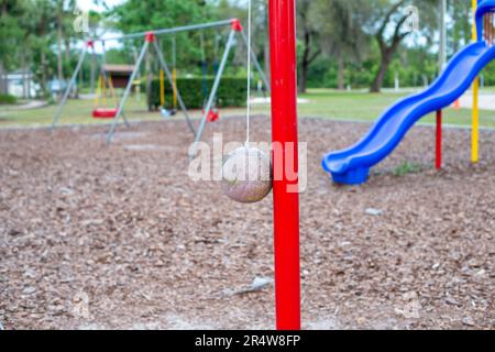 Plusieurs balançoires en plastique et en caoutchouc accrochées à des chaînes dans un parc pour enfants. Il y a une glissoire en plastique bleu à l'arrière-plan avec de grands arbres luxuriants et Banque D'Images