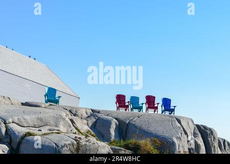 Rouge vif et bleu vide solide résine matériau Adirondack chaise sur le sol rocailleux avec des collines ondulantes surplombant l'océan et la plage. Banque D'Images
