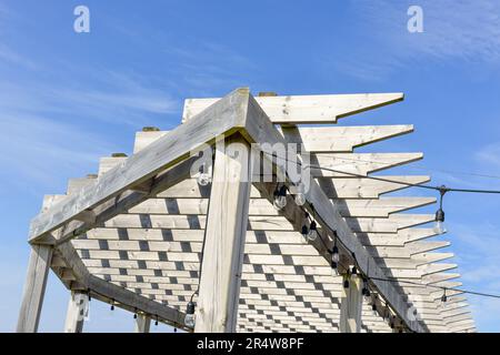 Toit de pergola en bois de couleur grise usé et abîmé avec un ciel bleu. L'abri de soleil extérieur a des lattes en bois dans un motif avec des bords pointés. Banque D'Images