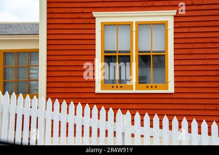 Un mur extérieur avec un parement horizontal en claquettes de cap de couleur orange et une double fenêtre suspendue. La fenêtre en verre vintage fermée a une garniture jaune. Banque D'Images