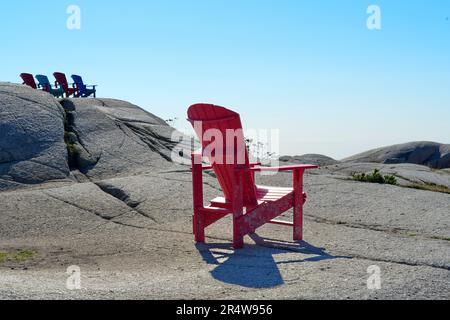 Une chaise Adirondack rouge vif et vide en résine robuste sur le sol rocailleux avec des collines ondulantes surplombant l'océan et la plage. Banque D'Images