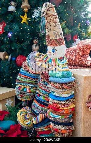 Une poupée yo yo-yo vintage en tissu matelassé coloré sous un arbre de Noël décoré. Le vieux jouet a un cône pour un chapeau avec un clown brodé Banque D'Images