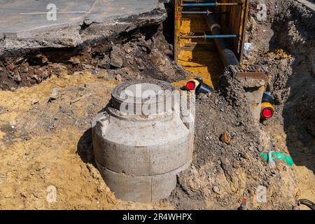 Un puits d'égout excavé pour réparation avec un trou d'homme en métal et de nouveaux tuyaux qui y sont reliés. Banque D'Images