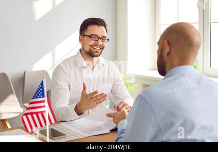 Consul souriant au bureau avec drapeau américain parlant à l'homme de son visa de voyage aux États-Unis Banque D'Images