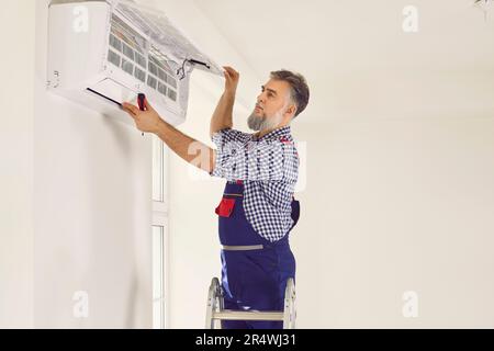 Électricien professionnel avec tournevis pour entretenir la climatisation moderne à l'intérieur. Banque D'Images