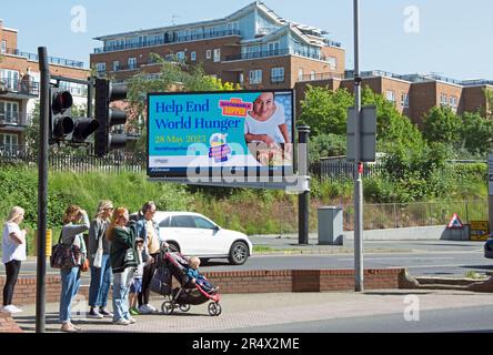 des piétons attendent à un passage à kingston, surrey, angleterre, devant un panneau d'affichage numérique annonçant la journée mondiale de la faim, 28 mai 2023 Banque D'Images