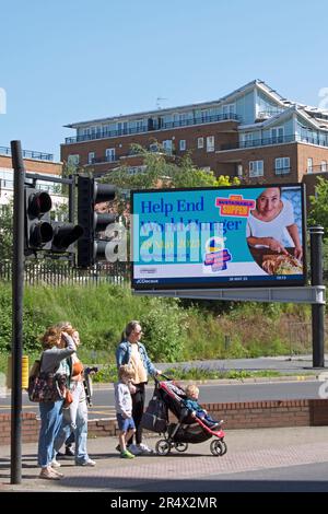 des piétons attendent à un passage à kingston, surrey, angleterre, devant un panneau d'affichage numérique annonçant la journée mondiale de la faim, 28 mai 2023 Banque D'Images