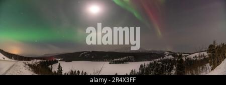 Vue panoramique d'aurora borealis, lumières nordiques vues au-dessus du paysage du nord du territoire canadien du Yukon en hiver avec des montagnes enneigées. Banque D'Images