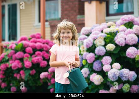 Joli petit garçon arrosoir fleurs avec arrosoir dans le jardin. Enfant habillé en été clair ferme et t-shirt coloré, souriant et s'amuser Banque D'Images
