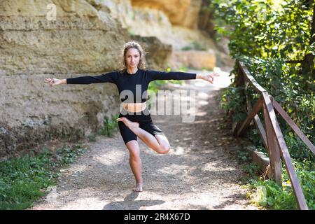 Jeune femme menant un mode de vie sain et pratiquant le yoga, faisant une variation de vrikshasana exercice, pose d'arbre avec les bras élevés sur les côtés, exerc Banque D'Images