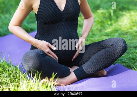 Une jeune femme enceinte menant un mode de vie sain et pratiquant le yoga est engagée dans la méditation assis dans une position de lotus, assis sur un tapis dans un Bla Banque D'Images