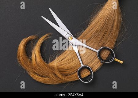 Ciseaux pour couper les cheveux et une mèche de cheveux blonds d'enfants coupée sur un fond de papier sombre Banque D'Images