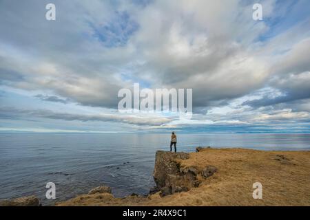 Vue prise de derrière d'une femme debout sur une falaise surplombant l'océan Atlantique sur la rive nord de l'Islande Banque D'Images