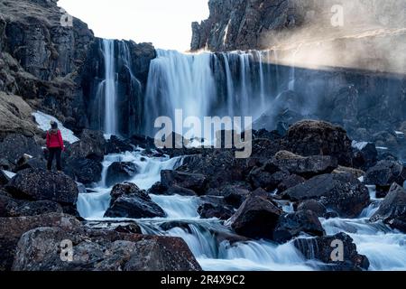 Femme debout près d'une cascade juste à l'extérieur de Seyðisfjörður dans les fjords est de l'Islande ; Islande orientale, Islande Banque D'Images