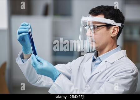 Portrait de la vue latérale d'un scientifique mâle portant un écran facial en laboratoire lors d'expériences avec un tube à essai Banque D'Images
