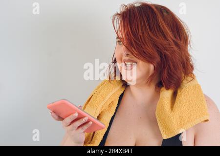 jeune femme hispanique latine d'origine argentine avec de courts cheveux rouges sourit en envoyant une note vocale par son téléphone sur fond blanc, espace de copie, Banque D'Images