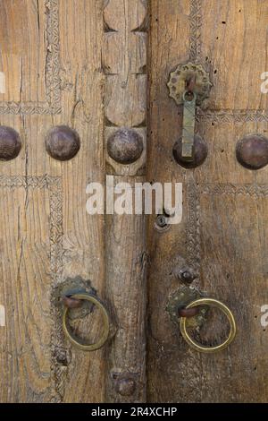 Porte en bois patiné avec poignées en laiton et rivets décoratifs sur la place POI Kalyon, Buhkara; Buhkara, Ouzbékistan Banque D'Images