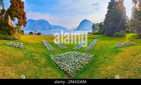 Pelouse verte, arbres luxuriants et parterres de fleurs ornementales dans le parc Ciani, situé sur la rive du lac de Lugano contre le Monte San Salvatore, Lugano, Suissela Banque D'Images