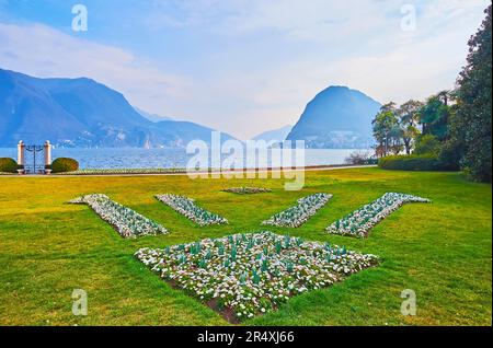 La pelouse verte et les parterres de fleurs ornementales de pâquerettes à Parco Ciani, situé sur la banque de Ceresio contre le Monte San Salvatore, Lugano, Suisse Banque D'Images