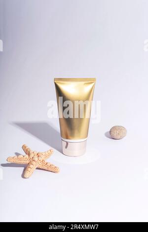 Tube de crème dorée et étoiles de mer sur fond blanc avec ombres dures. Crème solaire, concept de cosmétiques naturels. Gros plan. Banque D'Images