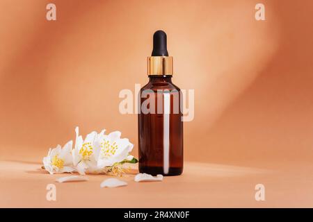 Bouteille de sérum cosmétique marron et fleurs de jasmin blanches sur fond beige neutre au soleil. Gros plan. Banque D'Images