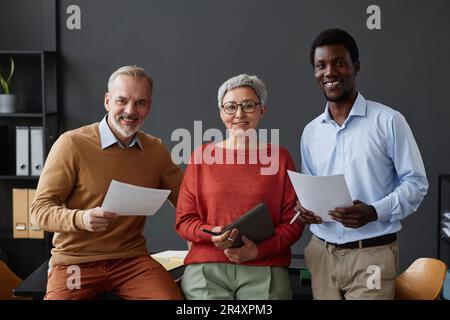 Un groupe diversifié de professionnels avec des employés seniors souriants qui regardent des caméras au bureau Banque D'Images
