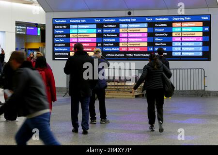Les gens qui attendent et qui coutent devant le panneau de départ de long Island Rail Road à Penn Station, New York, à l'heure de pointe. Banque D'Images