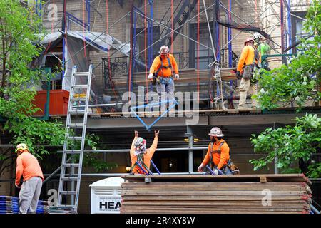 Des échafaudages, des ouvriers de construction déconstruisent des échafaudages et un abri de trottoir entourant un bâtiment en brique de maçonnerie à Manhattan, New York Banque D'Images