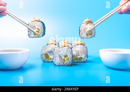 Morceaux de sushi roulés, avec fromage, daikon, poisson et sauce épicée, trempés dans de la sauce soja, sur fond bleu. Photo de haute qualité Banque D'Images