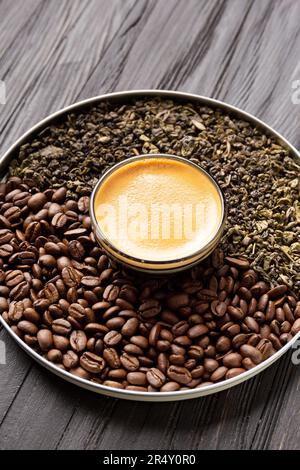Composition de feuilles de thé vert sec, de grains de café torréfiés dans une boîte ronde et de café dans une tasse sur fond de bois sombre. Banque D'Images