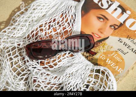 Lunettes de soleil élégantes et sac à ficelle avec magazine sur le sable Banque D'Images