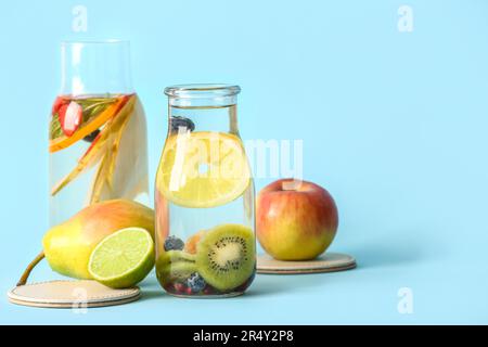 Bouteilles d'eau infusée avec différentes tranches de fruits sur fond bleu Banque D'Images