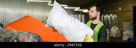 Vue latérale de l'homme barbu dans un gilet de protection et un sac à gants avec poubelle dans le conteneur pendant le travail dans la station d'élimination des déchets, tri des déchets et Banque D'Images