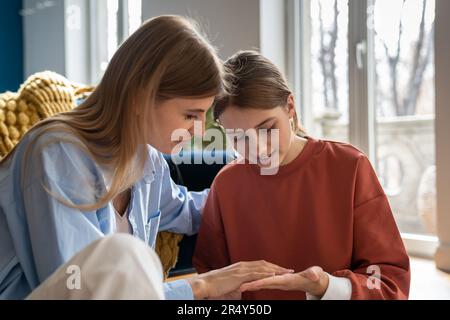 Mère compatissante touchant affectueusement la main de fille communiquant doucement sur les sujets délicats de l'adolescence Banque D'Images