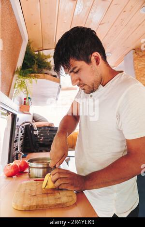 Latin homme préparant le repas dans la cuisine de sa camionnette. Vacances en minibus et aventure en plein air en été. Concept de style de vie nomade Banque D'Images