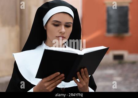 Jeune nun lisant la Bible près de bâtiment à l'extérieur Banque D'Images