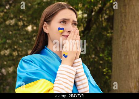 Jeune femme ukrainienne émotive avec des mains clashed dehors, espace pour le texte Banque D'Images