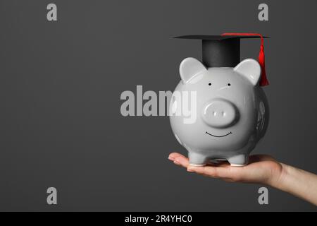 Femme tenant une tirelire et un chapeau de graduation sur fond gris foncé, gros plan avec un espace pour le texte. Concept de bourse Banque D'Images