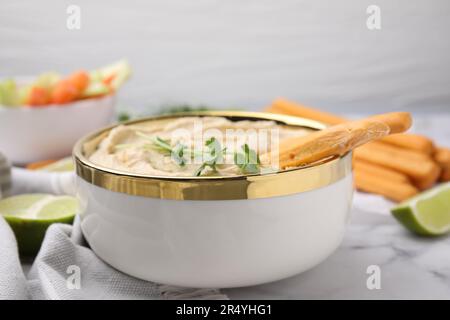 Délicieux houmous avec bâtonnets de grissini servis sur une table en marbre blanc, en gros plan Banque D'Images