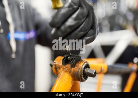 Entretien d'un vélo: Inconnu homme utilisant des gants de protection pour démonter un vélo orange dans son atelier de réparation. Banque D'Images