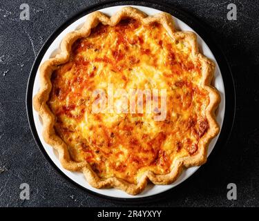 quiche de petit déjeuner moelleuse avec fromage et bacon dans un plat sur une table en béton sombre, vue horizontale depuis le dessus, plat, gros plan Banque D'Images