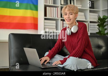 Portrait d'un jeune homme indépendant gay asiatique créatif et confiant travaille de la maison, en utilisant son ordinateur portable sur un canapé dans le salon. Banque D'Images