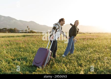 Un jeune couple épris inspiré regarde le plan de vie à l'avenir. Ils sont debout avec une valise et ukulele, tenant les mains. Recherche d'une nouvelle patrie. Banque D'Images